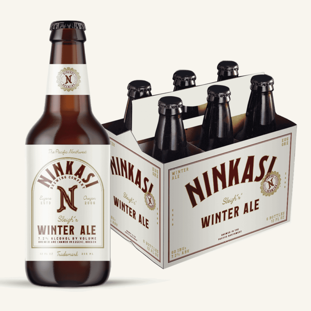 A bottle of Ninkasi "Sleigh'r Winter Ale" with a 7.2% alcohol by volume indication, next to a six-pack box of the same ale. The bottle and box have the Ninkasi Brewing Company logo and indicate it's brewed in Eugene, Oregon. The design is predominantly white with gold and maroon accents, featuring the words "The Pacific Northwest" on the bottle and "60 IBU" on the box.